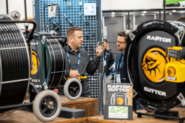 APS team member demonstrating the Raptor Cutter system to an attendee at a trade show, highlighting drain cleaning and pipe rehabilitation equipment